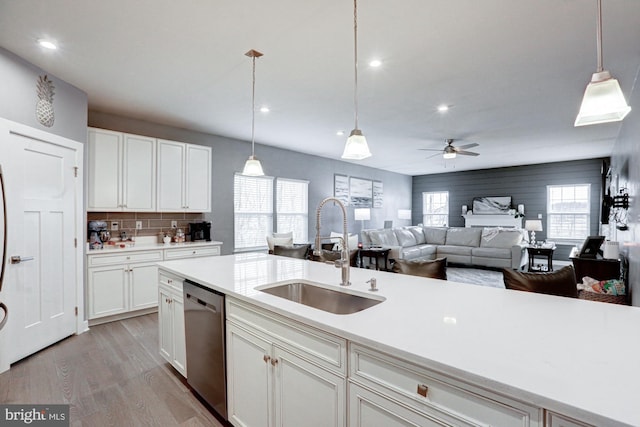 kitchen featuring dishwasher, sink, white cabinets, hanging light fixtures, and light hardwood / wood-style flooring