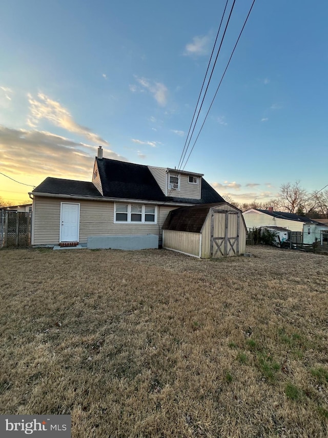 back house at dusk featuring a yard and a shed