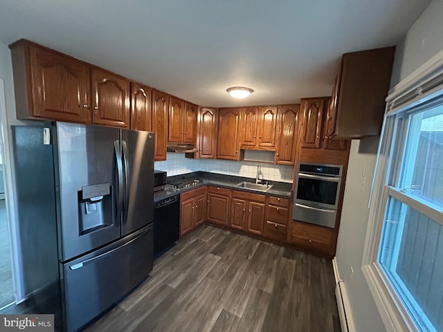 kitchen featuring a baseboard radiator, sink, backsplash, stainless steel appliances, and dark wood-type flooring