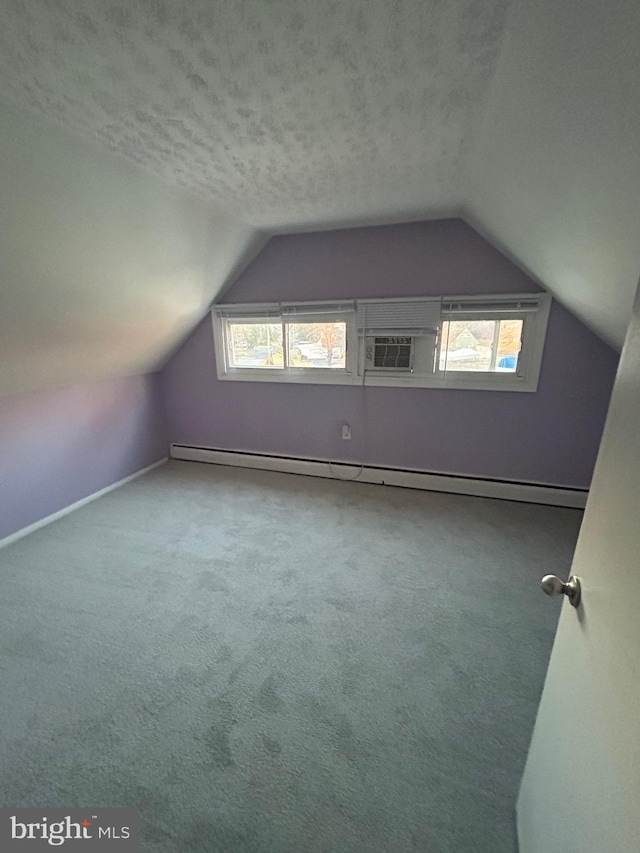 additional living space featuring a baseboard radiator, vaulted ceiling, a healthy amount of sunlight, and a textured ceiling