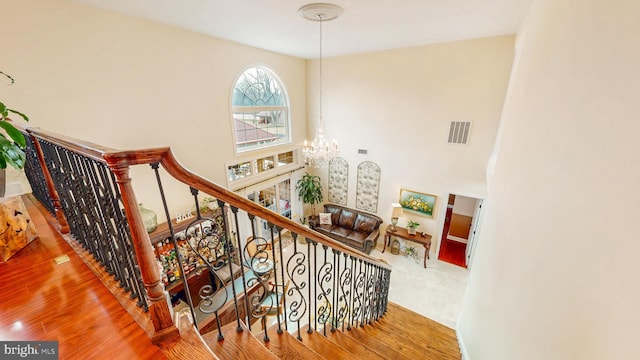 stairs featuring a chandelier, a high ceiling, wood finished floors, and visible vents