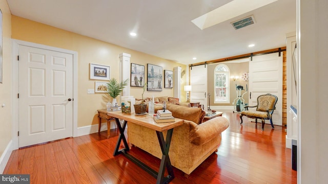 living area featuring a skylight, wood finished floors, visible vents, and a barn door