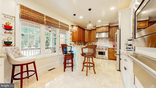 kitchen with a breakfast bar, under cabinet range hood, stainless steel appliances, and brown cabinetry