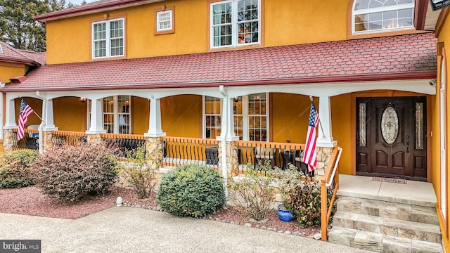 doorway to property featuring covered porch, a tiled roof, and stucco siding