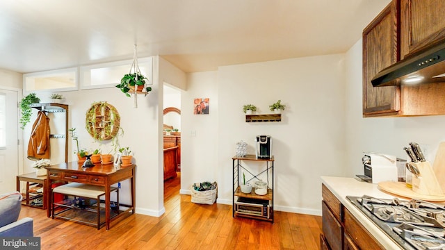 kitchen featuring light wood finished floors, baseboards, light countertops, stainless steel gas cooktop, and exhaust hood