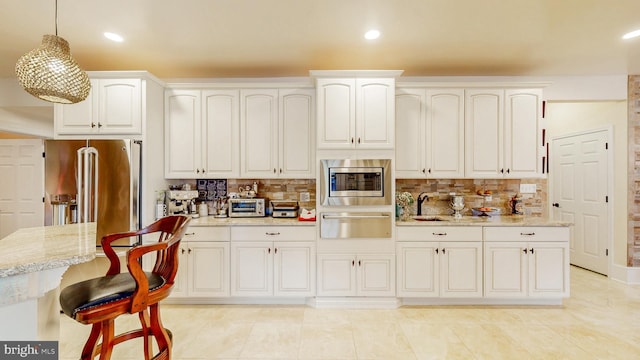 kitchen featuring light stone counters, stainless steel appliances, a sink, a warming drawer, and decorative light fixtures