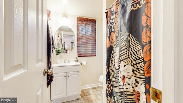 bathroom featuring toilet, vanity, stone tile flooring, and baseboards