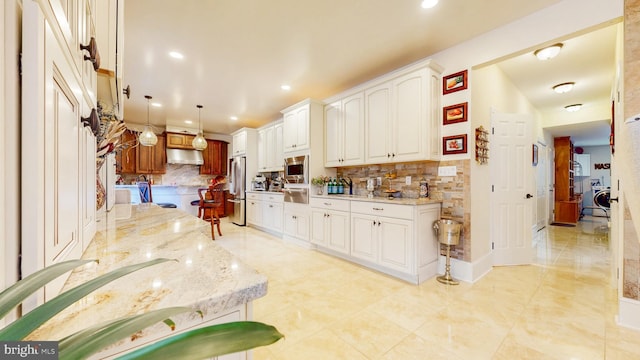 kitchen with white cabinets, appliances with stainless steel finishes, decorative light fixtures, light stone countertops, and a kitchen bar