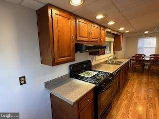 kitchen with sink, black range oven, ventilation hood, light wood-type flooring, and a drop ceiling