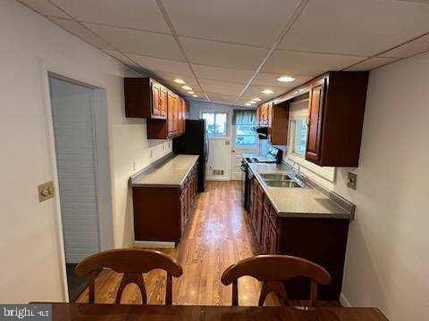 kitchen with sink, a paneled ceiling, light wood-type flooring, black refrigerator, and stove