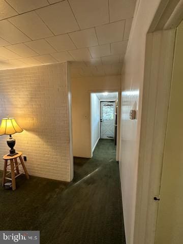 hallway featuring brick wall and dark carpet