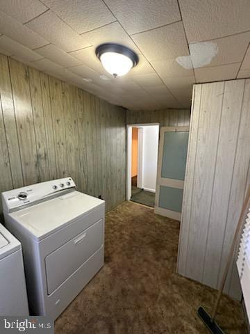 clothes washing area with wood walls, washing machine and dryer, and dark colored carpet