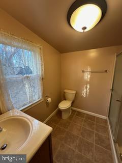 bathroom featuring vanity, toilet, a shower with shower door, and vaulted ceiling