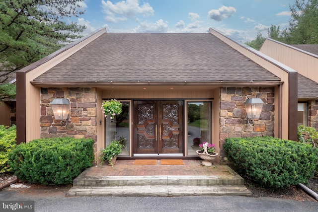 property entrance featuring stone siding and roof with shingles