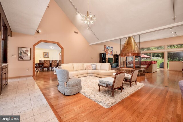 living area featuring arched walkways, high vaulted ceiling, light wood-style flooring, and an inviting chandelier