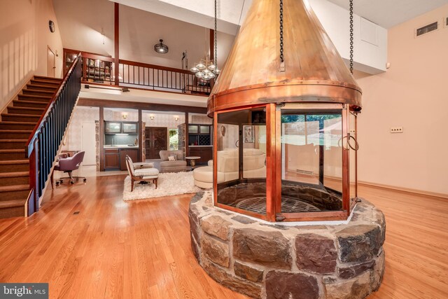 living area with wood finished floors, a towering ceiling, visible vents, stairs, and an inviting chandelier