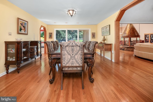 dining space with arched walkways, baseboards, and light wood-style floors