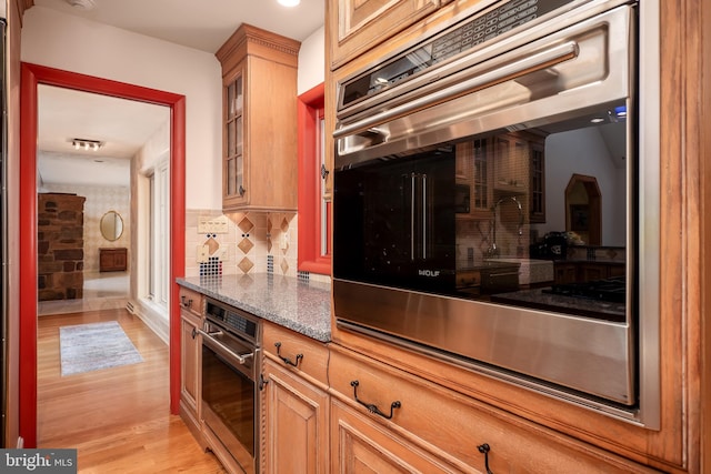 kitchen featuring tasteful backsplash, glass insert cabinets, light wood-style floors, and dark stone countertops