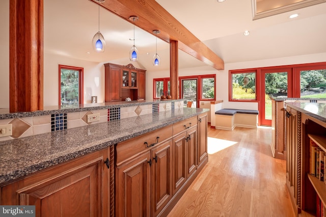 kitchen with brown cabinetry, light wood-type flooring, dark stone counters, and backsplash