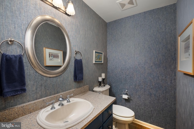 bathroom with vanity, toilet, and wallpapered walls