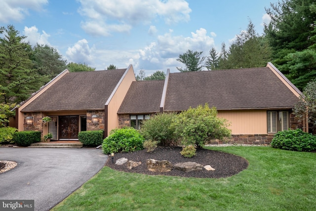 view of front of house with aphalt driveway, stone siding, a shingled roof, and a front lawn