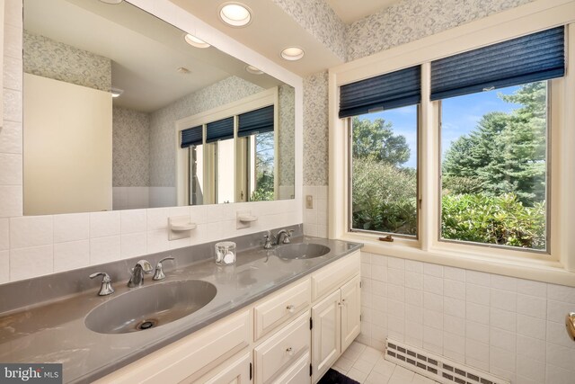 full bathroom with wallpapered walls, tile walls, a sink, and wainscoting