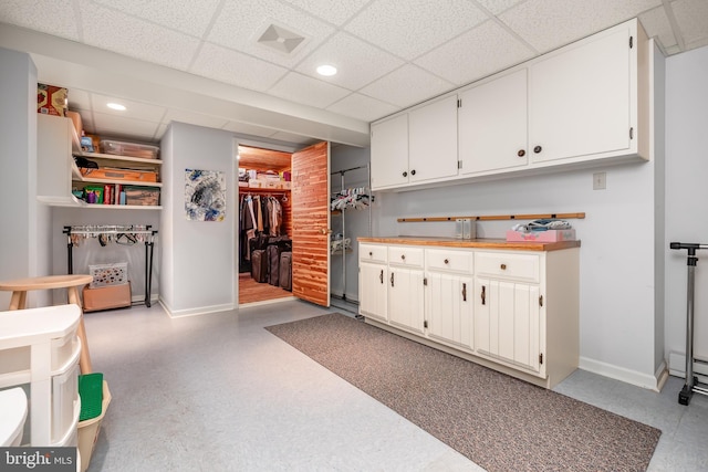 interior space featuring white cabinetry, baseboards, a drop ceiling, and recessed lighting