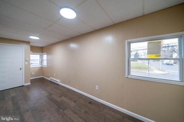 empty room featuring dark hardwood / wood-style flooring, a baseboard heating unit, and a paneled ceiling