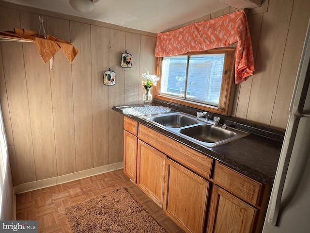 kitchen with white refrigerator, light parquet flooring, sink, and wooden walls