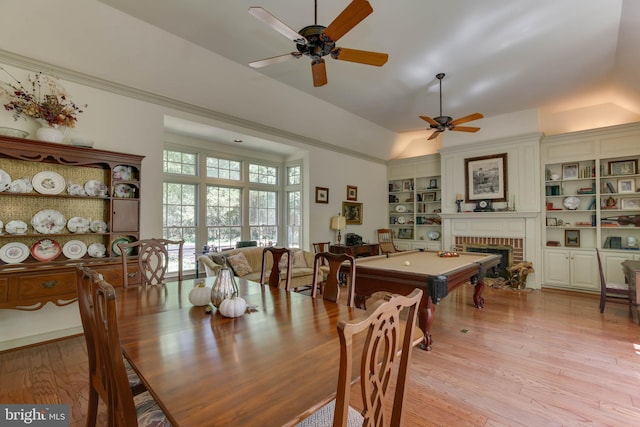 dining room featuring vaulted ceiling, built in features, billiards, a brick fireplace, and light wood-type flooring