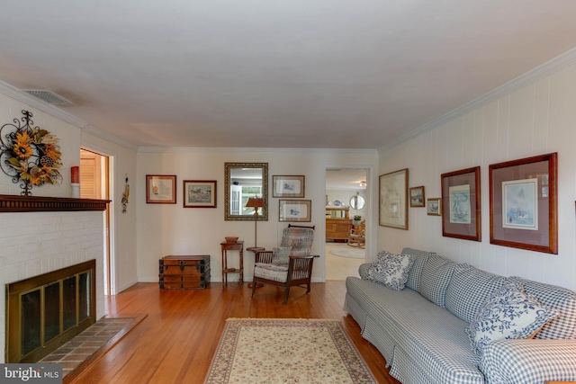 living room with a brick fireplace, ornamental molding, and light wood-type flooring