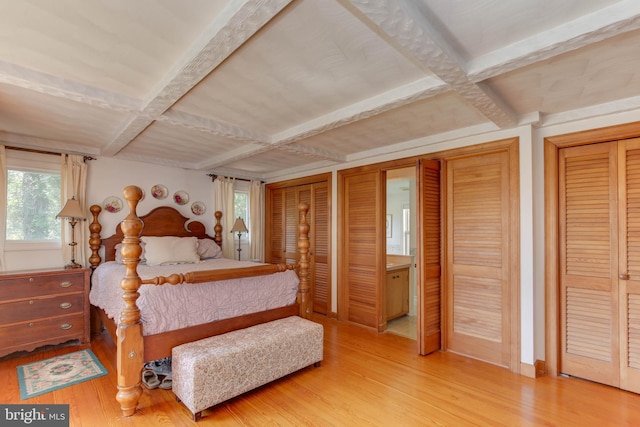 bedroom featuring hardwood / wood-style flooring, coffered ceiling, two closets, and beamed ceiling