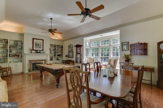 dining space featuring built in features, ceiling fan, ornamental molding, light hardwood / wood-style floors, and a brick fireplace