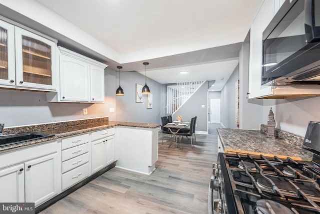 kitchen with pendant lighting, white cabinetry, light hardwood / wood-style floors, gas range, and dark stone counters