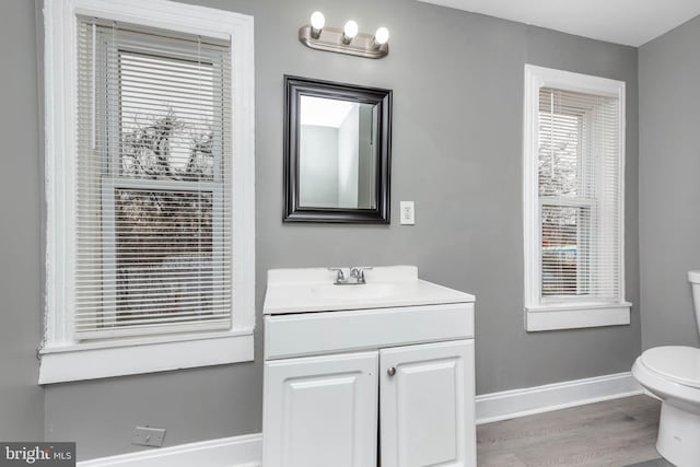 bathroom featuring hardwood / wood-style flooring, vanity, a healthy amount of sunlight, and toilet