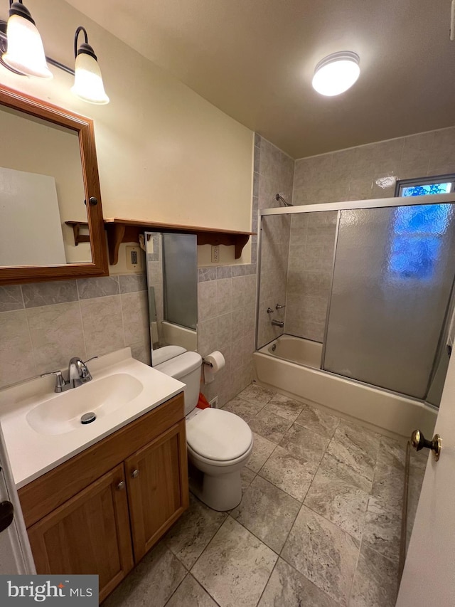 full bathroom featuring vanity, tile walls, enclosed tub / shower combo, and toilet