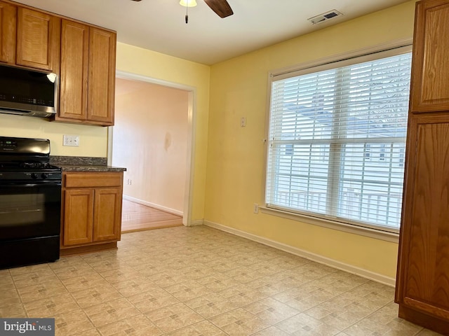 kitchen with dark countertops, visible vents, stainless steel microwave, black gas range oven, and brown cabinetry