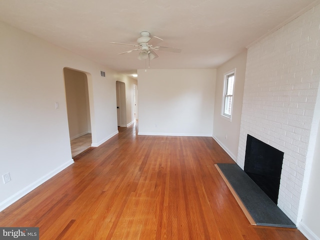 unfurnished living room featuring hardwood / wood-style flooring, ceiling fan, and a brick fireplace