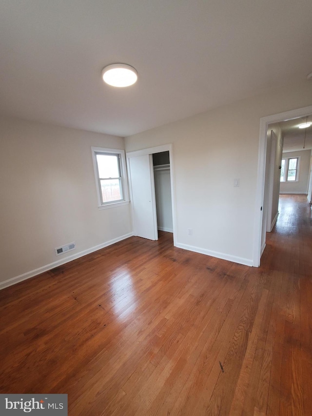 unfurnished bedroom with a closet, wood-type flooring, and multiple windows