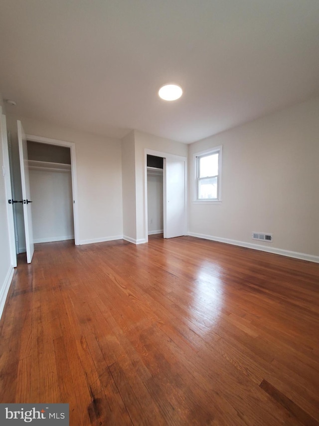 unfurnished bedroom featuring hardwood / wood-style flooring and two closets