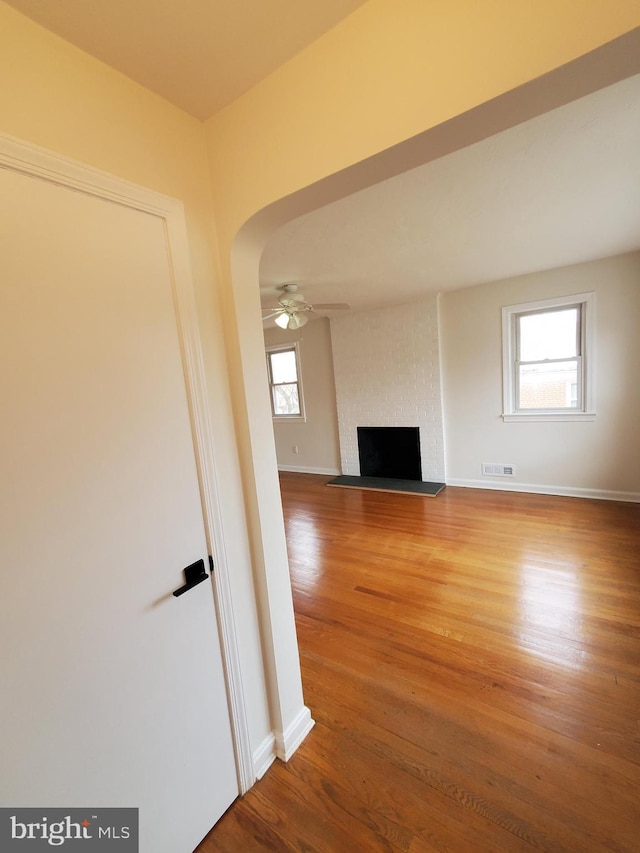 unfurnished living room with a brick fireplace, wood-type flooring, and ceiling fan