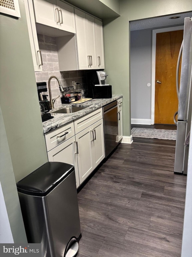 kitchen featuring white cabinets, decorative backsplash, dark wood-type flooring, stainless steel appliances, and a sink