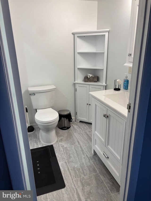 half bathroom featuring baseboards, vanity, and toilet