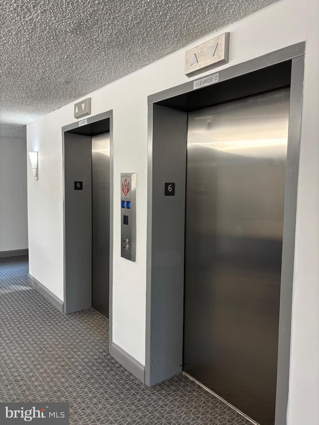 corridor with elevator, carpet flooring, and a textured ceiling