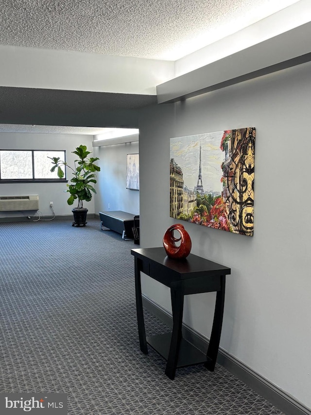 hallway with baseboards, dark colored carpet, a textured ceiling, and a wall mounted air conditioner