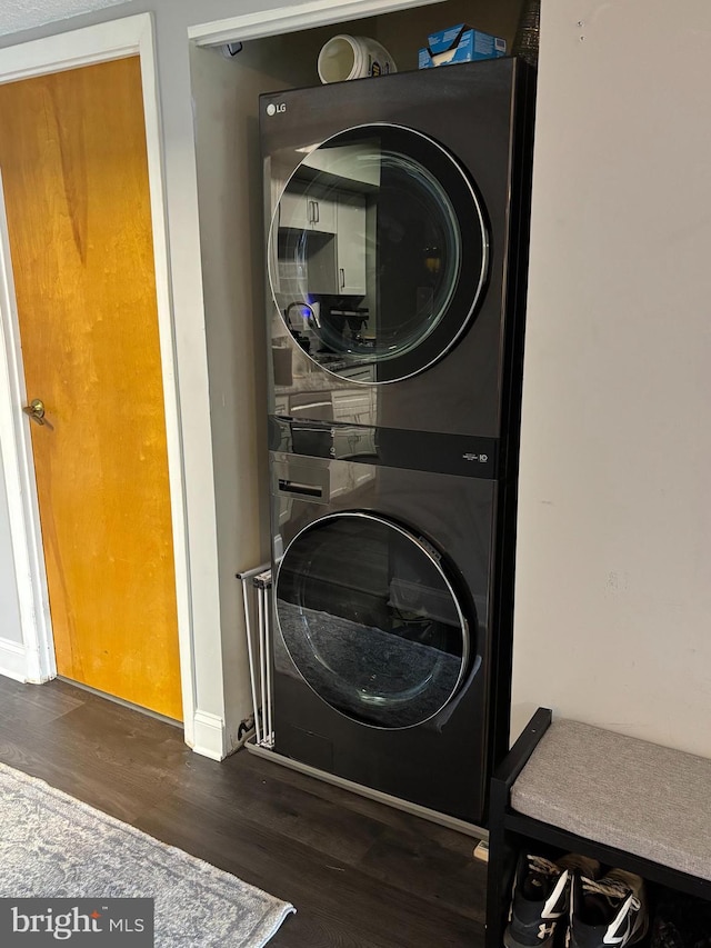 clothes washing area featuring wood finished floors, stacked washer and clothes dryer, baseboards, and laundry area