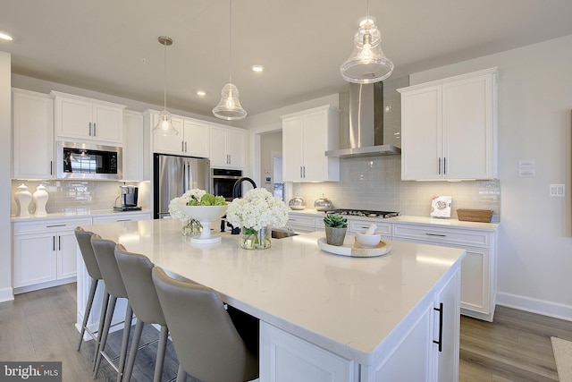 kitchen featuring white cabinetry, stainless steel appliances, an island with sink, and wall chimney exhaust hood