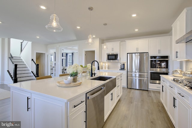 kitchen featuring light hardwood / wood-style flooring, hanging light fixtures, an island with sink, stainless steel appliances, and white cabinets