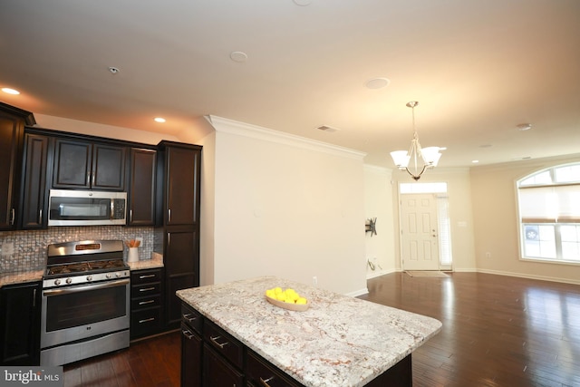 kitchen with appliances with stainless steel finishes, dark hardwood / wood-style floors, a kitchen island, and backsplash