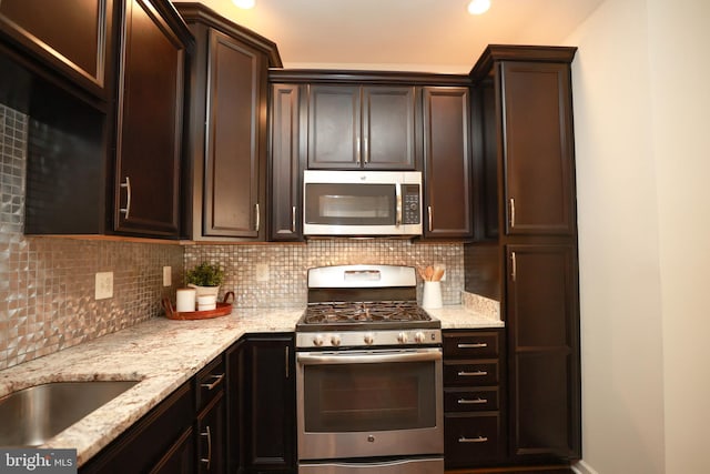 kitchen with light stone counters, dark brown cabinetry, stainless steel appliances, and backsplash